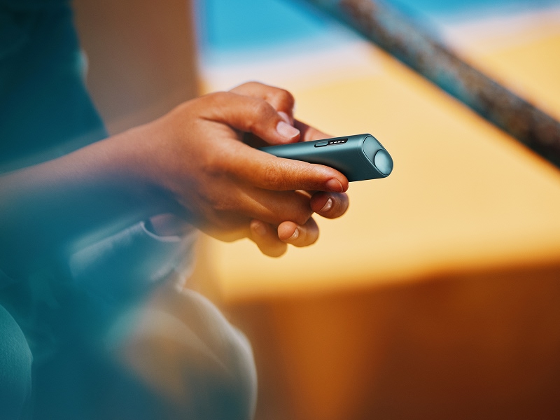 A person holding an IQOS ILUMA i ONE color Breeze Blue with their hands